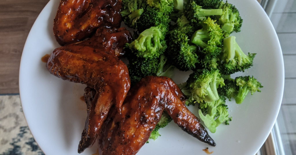 Recipes 9 a white plate with three saucy chicken wings and steamed broccoli florets