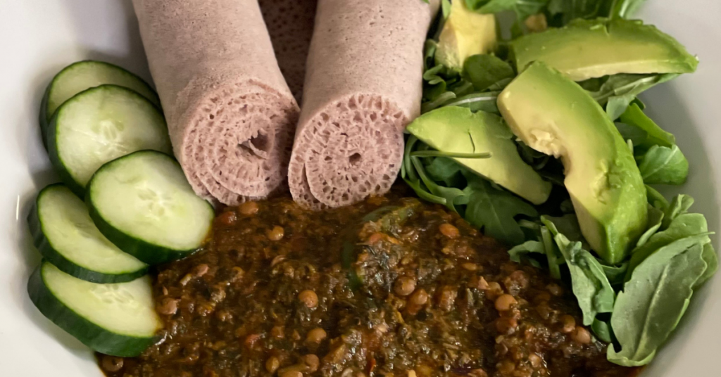 Recipes 7 a bowl with lentil stew, sliced cucumbers, avocado, and rolls of injera